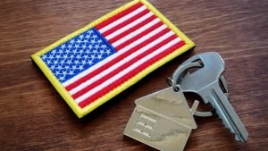 A U.S. flag patch beside a house key with a house-shaped key chain on a wooden table