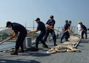 Sailors hauling heavy mooring lines across a ship's deck