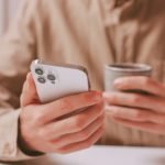 man holding an iPhone while drinking coffee