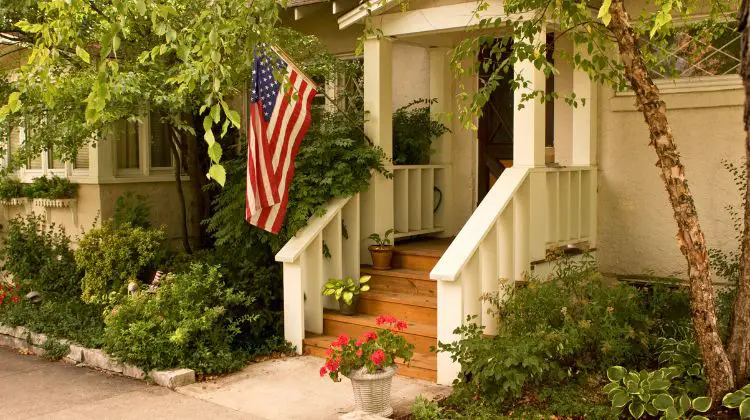 front of home with flowers and US flag