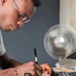 man sitting at desk taking notes in front of his computer