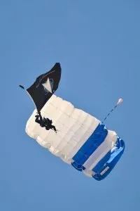 A skydiver descends under a blue and white U.S. Space Force parachute.