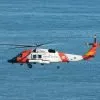 white and orange US Coast Guard helicopter flying over the sea during daytime