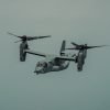 A gray osprey aircraft flies in a cloudy sky.
