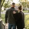 A couple stands on their front porch steps looking out at a tree-lined street, the man holding an opened envelope